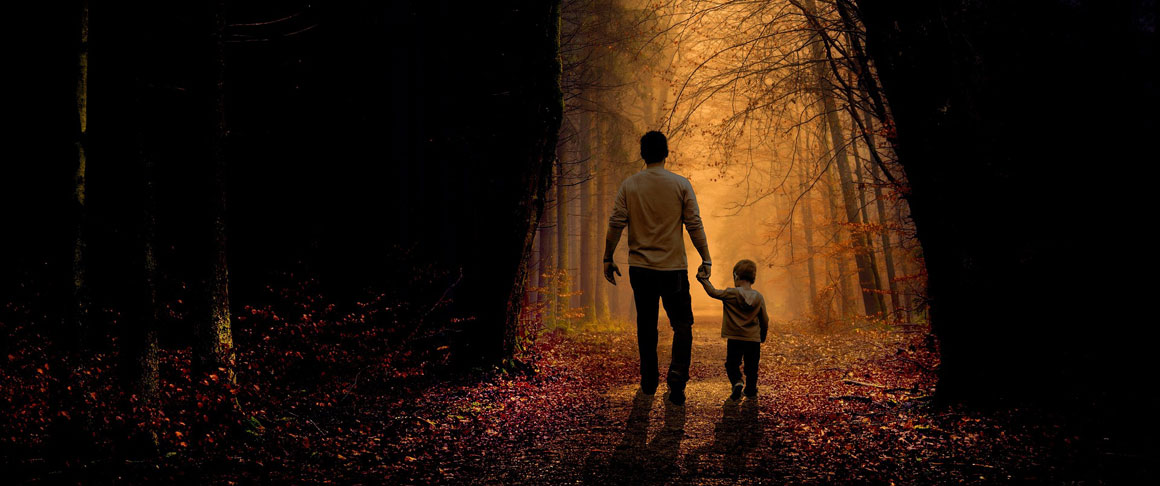 A father and son holding hands in while walking in the woods