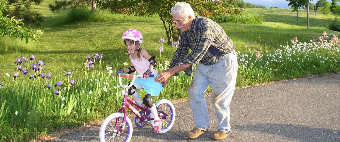An older man helps a young girl learn to ride a bike