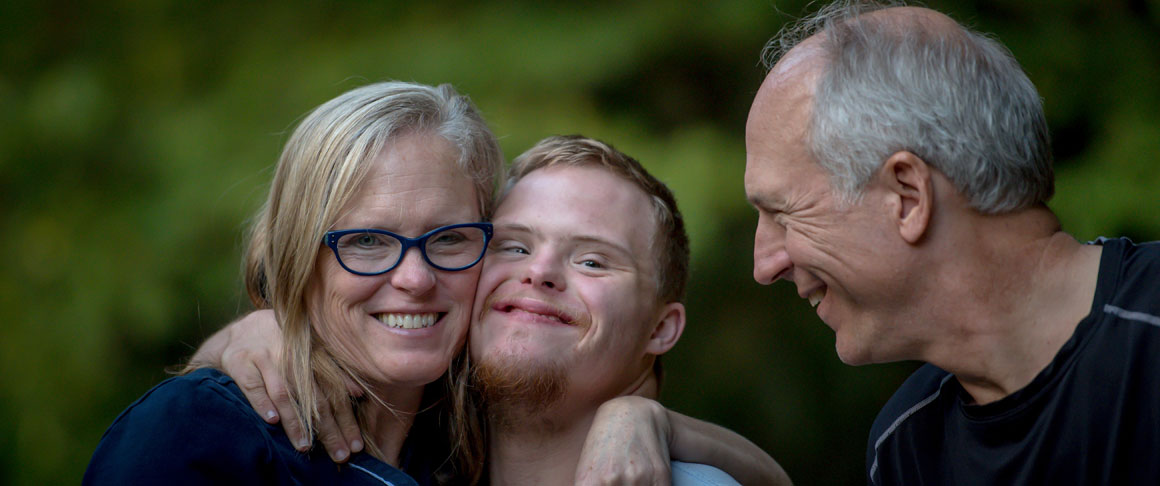 A young man with down syndrome and an older couple all smiling